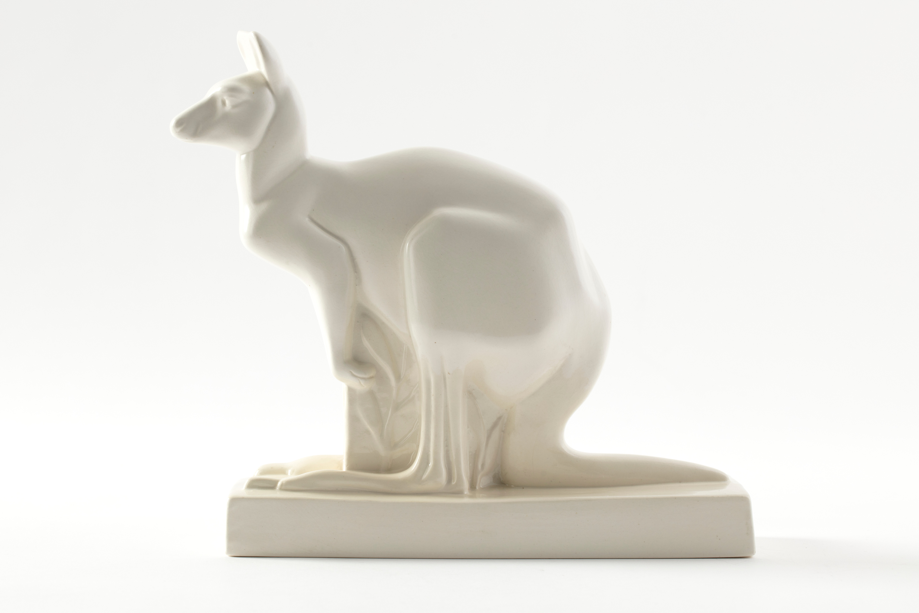 White earthenware kangaroo on a white studio background. The kangaroo has a minimalist form, sits on a rectangular base, and is lit by soft lighting.